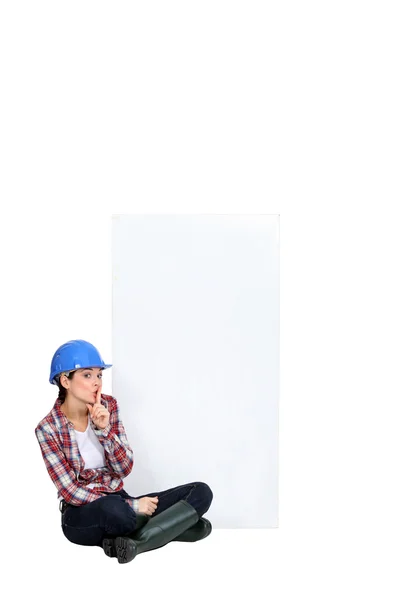 Tradeswoman sitting cross-legged by an empty sign — Stock Photo, Image