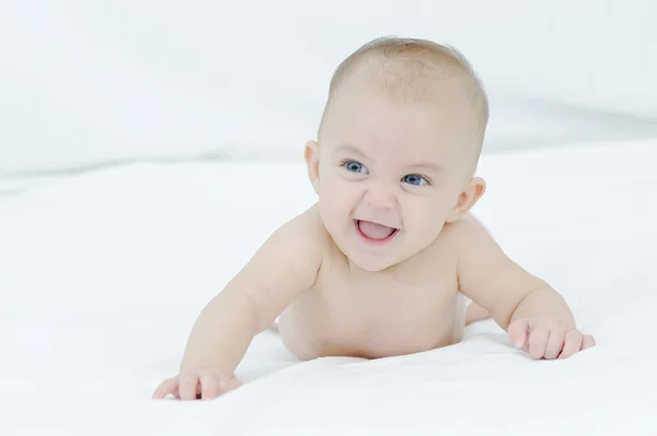 Joyeux enfant souriant jouant sur un lit blanc — Photo