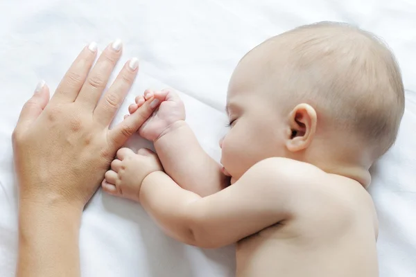 Дитина спить поруч зі своєю матір'ю, тримаючи палець — стокове фото