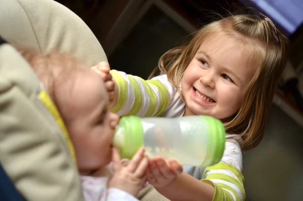 Menina jovem alimenta sua irmã bebê em uma cadeira alta — Fotografia de Stock