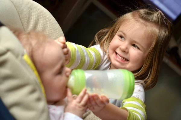 stock image Young girl feeds her baby sister in a highchair