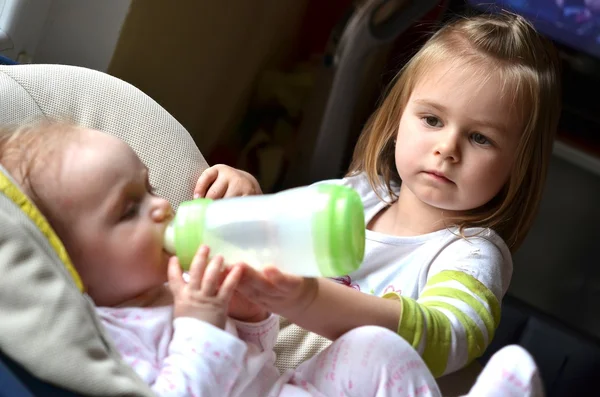 Young girl feeds her baby sister in a highchair — Stock Photo, Image