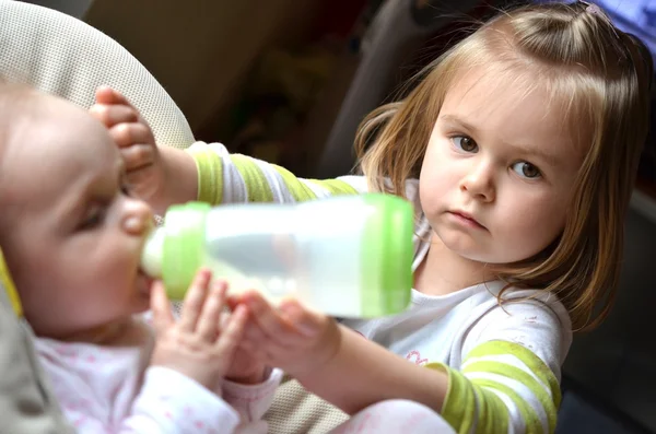 Menina jovem alimenta sua irmã bebê em uma cadeira alta — Fotografia de Stock