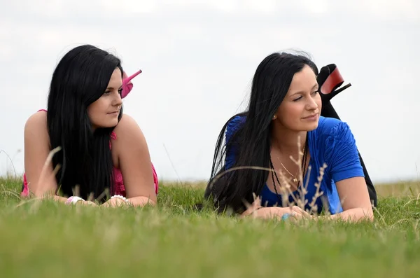 Zwei junge schöne Mädchen, die auf einem grünen Hintergrund liegen — Stockfoto