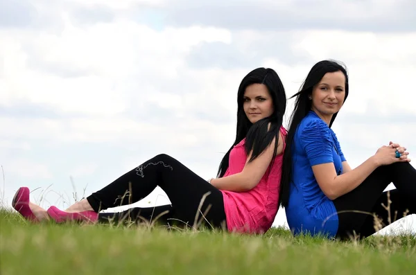 Duas meninas bonitas jovens sentadas em um fundo de natureza verde — Fotografia de Stock