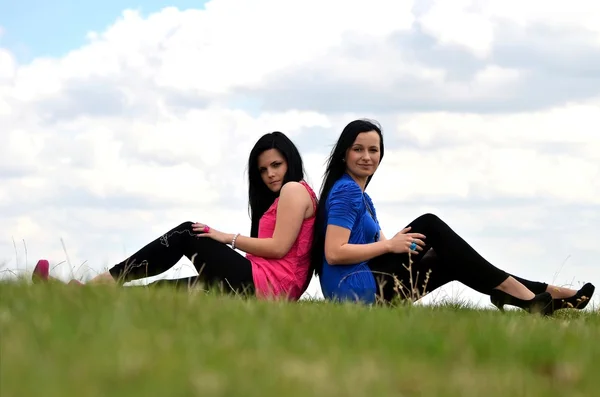 Twee jonge mooie meisjes zitten op een achtergrond van groene natuur — Stockfoto