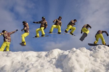 Güneşli bir günde yüksek dağlara atlayan snowboardcu..