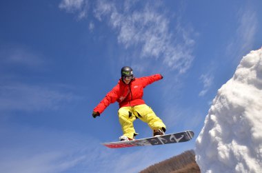 Güneşli bir günde yüksek dağlara atlayan snowboardcu..