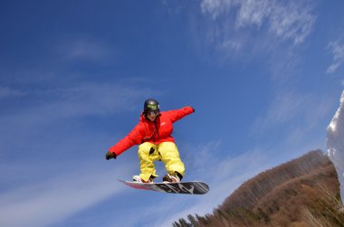 Güneşli bir günde yüksek dağlara atlayan snowboardcu..