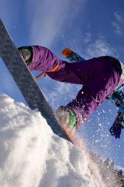 Güneşli bir günde yüksek dağlara atlayan snowboardcu..