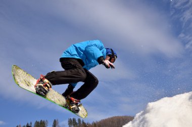 Güneşli bir günde yüksek dağlara atlayan snowboardcu..