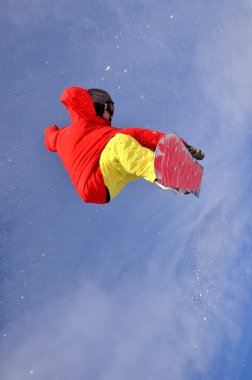 Güneşli bir günde yüksek dağlara atlayan snowboardcu..