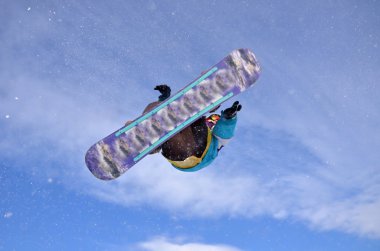 Güneşli bir günde yüksek dağlara atlayan snowboardcu..