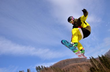 Güneşli bir günde yüksek dağlara atlayan snowboardcu..