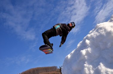 Güneşli bir günde yüksek dağlara atlayan snowboardcu..