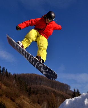 Güneşli bir günde yüksek dağlara atlayan snowboardcu..