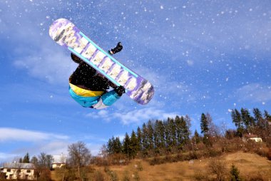 Güneşli bir günde yüksek dağlara atlayan snowboardcu..