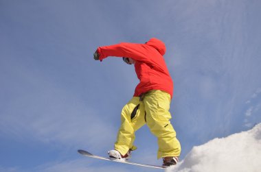 Güneşli bir günde yüksek dağlara atlayan snowboardcu..