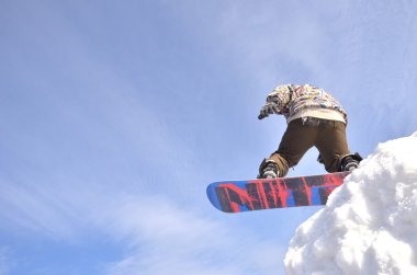 Güneşli bir günde yüksek dağlara atlayan snowboardcu..