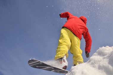 Güneşli bir günde yüksek dağlara atlayan snowboardcu..