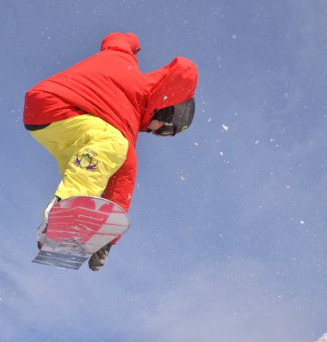 Güneşli bir günde yüksek dağlara atlayan snowboardcu..