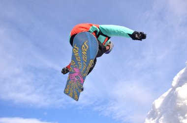 Güneşli bir günde yüksek dağlara atlayan snowboardcu..