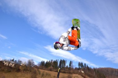 Güneşli bir günde yüksek dağlara atlayan snowboardcu..