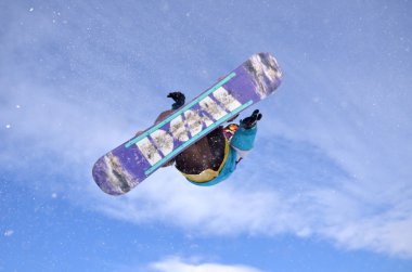 Güneşli bir günde yüksek dağlara atlayan snowboardcu..