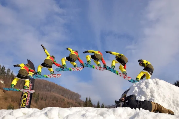 Güneşli bir günde yüksek dağlara atlayan snowboardcu..