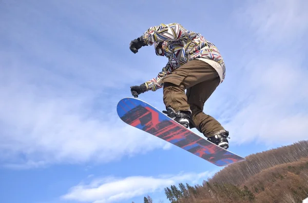 Snowboardos ugrás magas hegyekben a napsütéses napon. — Stock Fotó