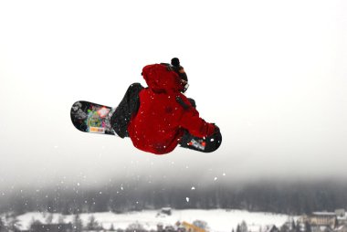 Güneşli bir günde yüksek dağlara atlayan snowboardcu..