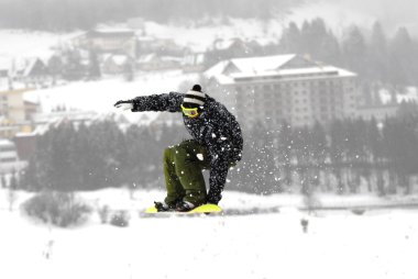 Güneşli bir günde yüksek dağlara atlayan snowboardcu..