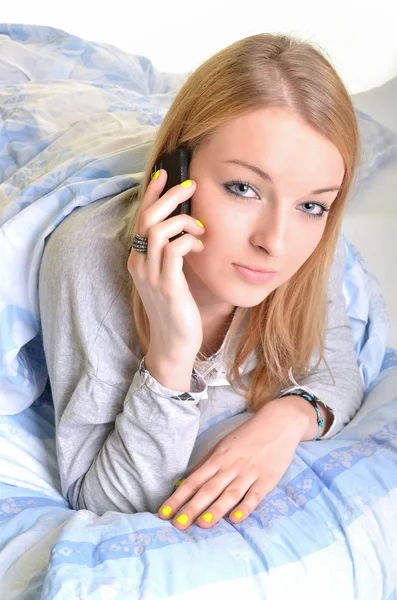 Aantrekkelijke jonge vrouw praten over de telefoon terwijl liggend in het bed. — Stockfoto