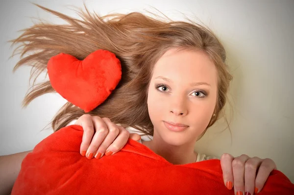 Ελκυστική νεαρή γυναίκα που αγκαλιάζει το σχήμα καρδιάς μαξιλάρι. όλα σε άσπρο φόντο — Φωτογραφία Αρχείου