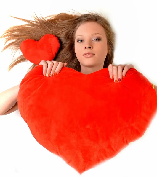 Uma jovem atraente abraçando um travesseiro em forma de coração. Tudo sobre fundo branco — Fotografia de Stock