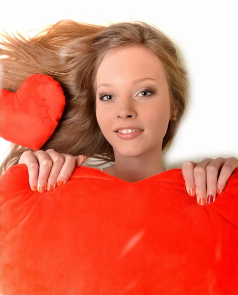 Çekici genç kadın kalp şeklinde yastık kucaklıyor. Tüm beyaz zemin üzerine — Stok fotoğraf