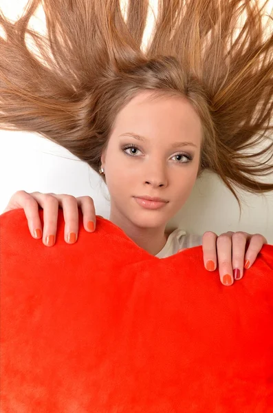 Çekici genç kadın kalp şeklinde yastık kucaklıyor. Tüm beyaz zemin üzerine — Stok fotoğraf