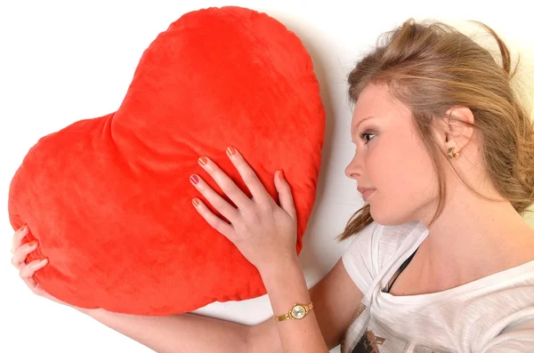 Atractiva joven mujer abrazando almohada en forma de corazón. Todo sobre fondo blanco —  Fotos de Stock