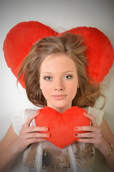 Приваблива молода жінка обіймає подушку у формі серця. Все на білому тлі — стокове фото