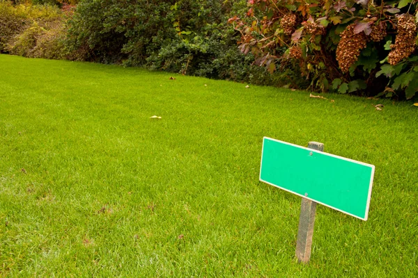 Green grass with a sign and a bush, sideview horizontal shot Royalty Free Stock Photos