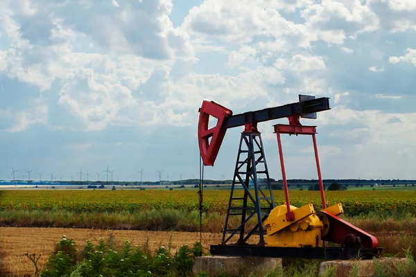 stock image Old oil rig with sunflower field and modern wind generators