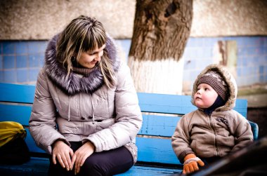 Mum and the son on a bench in a court yard clipart