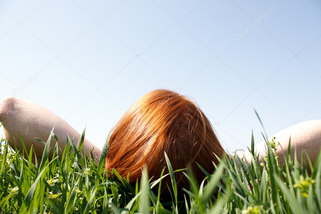 Red haired woman laying in grass looking up