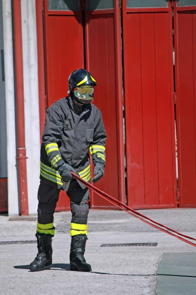 Strażak podczas unrolls węża pożarowego do gaszenia płomieni — Zdjęcie stockowe