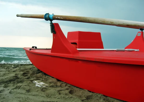 Röd beredskapsbåt med trä åror längs stranden — Stockfoto
