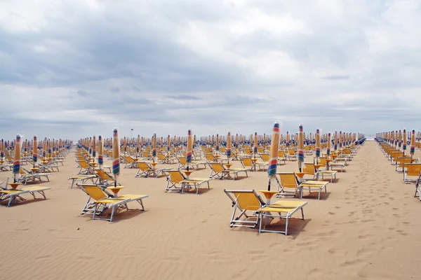 Sedie, sdraio e ombrelloni chiusi in una linea lungo la spiaggia sabbiosa i — Foto Stock
