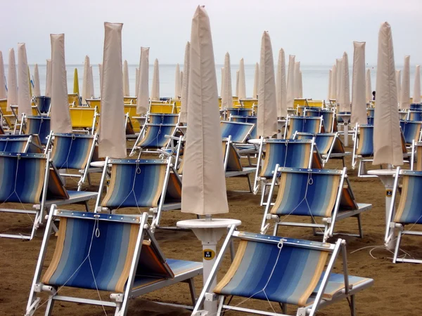 Sun beds and umbrellas closed in a deserted sandy beach — Stock Photo, Image