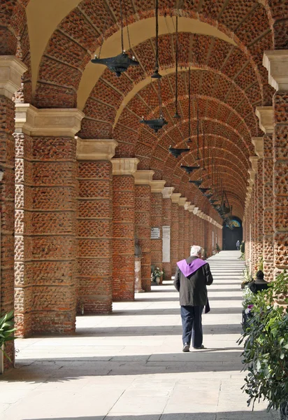 Sacerdote caminhando ao longo das arcadas de um cemitério — Fotografia de Stock