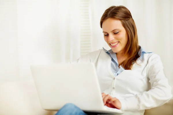 Мила молода жінка посміхається і працює на ноутбуці — стокове фото