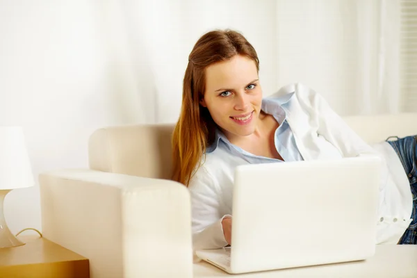 Mujer atractiva tumbada en el sofá con un ordenador portátil — Foto de Stock